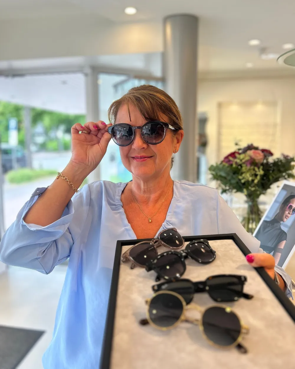 Eine Frau probiert eine Sonnenbrille, vor ihr ein Tablett mit weiteren Sonnenbrillen