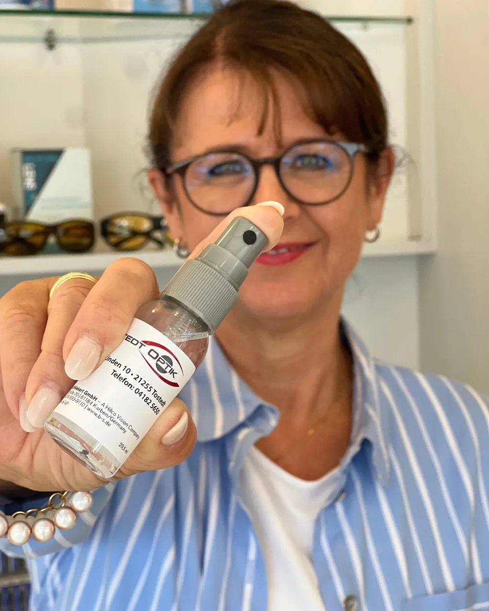 Eine Augenoptikerin hält ein kleines Reinigungsspray mit dem Logo von Dreppenstedt Optik in die Kamera